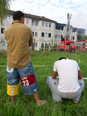 Zwei Männer sitzen vor dem brennenden Flüchtlingswohnheim in Stuttgart.