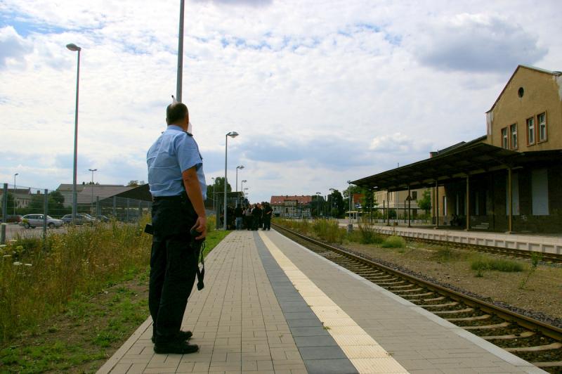 Die Demo ist zuende; die Teilnehmer_innen warten auf den Zug, während ein Polizist die Menschen im Auge behält und Fotos anfertigt.
