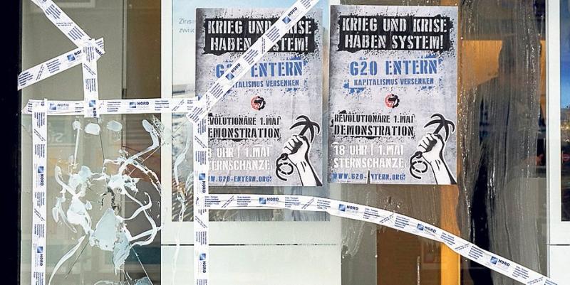 Eine eingeschlagene Scheibe der Filiale der Deutschen Bank an der Veringstraße. Daneben hängen Plakate für die 1.-Mai-Demonstration.